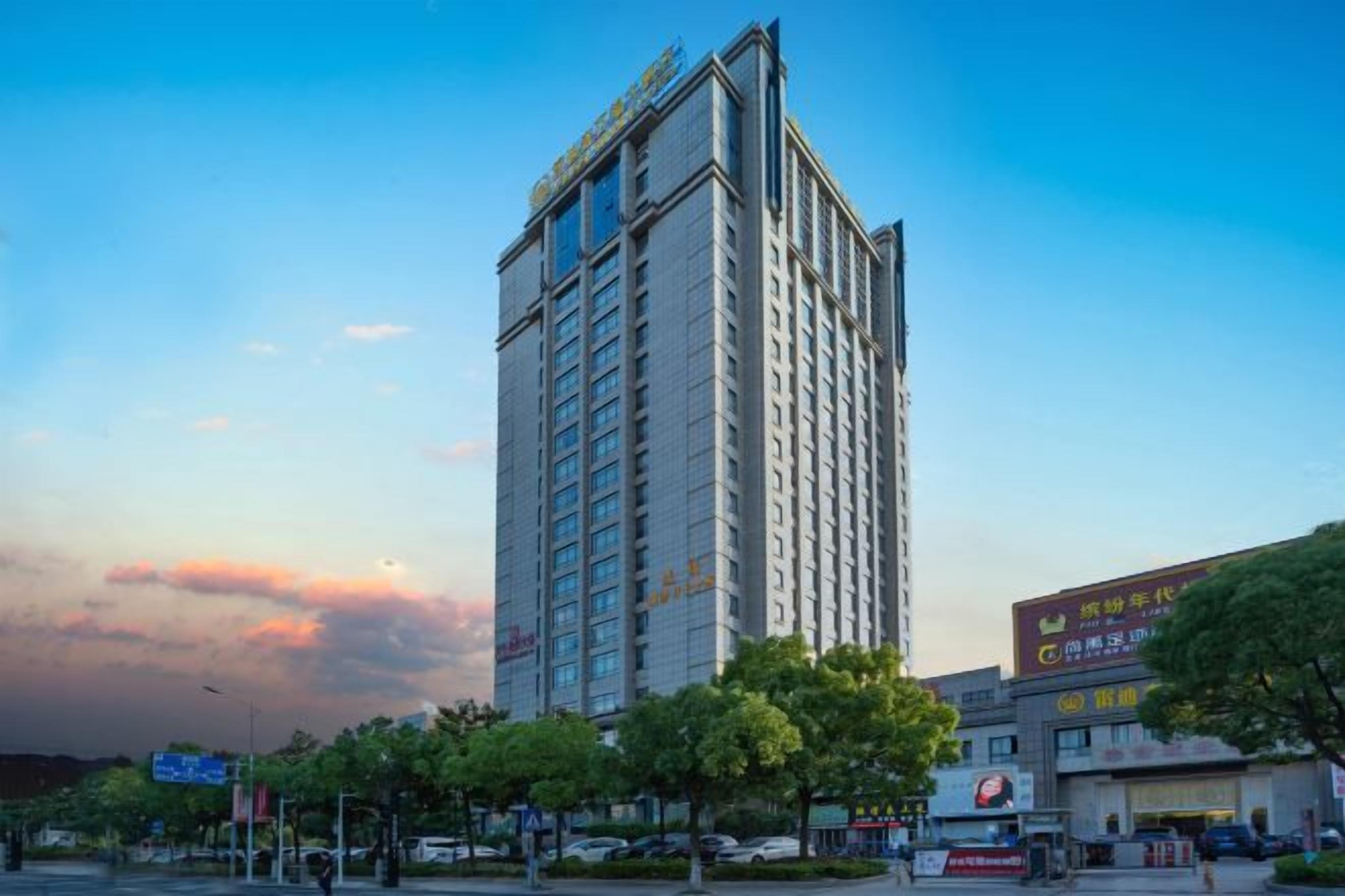 A high-rise hotel with multiple floors, a prominent entrance, and a surrounding urban environment with trees and storefronts.