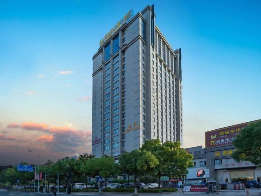 A high-rise hotel with multiple floors, a prominent entrance, and a surrounding urban environment with trees and storefronts.