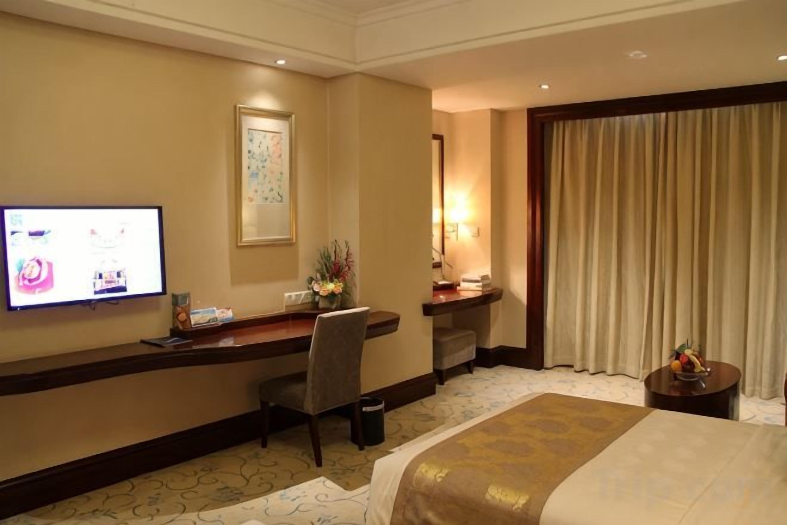 A hotel room with a bed, desk, television, and a large window with curtains.