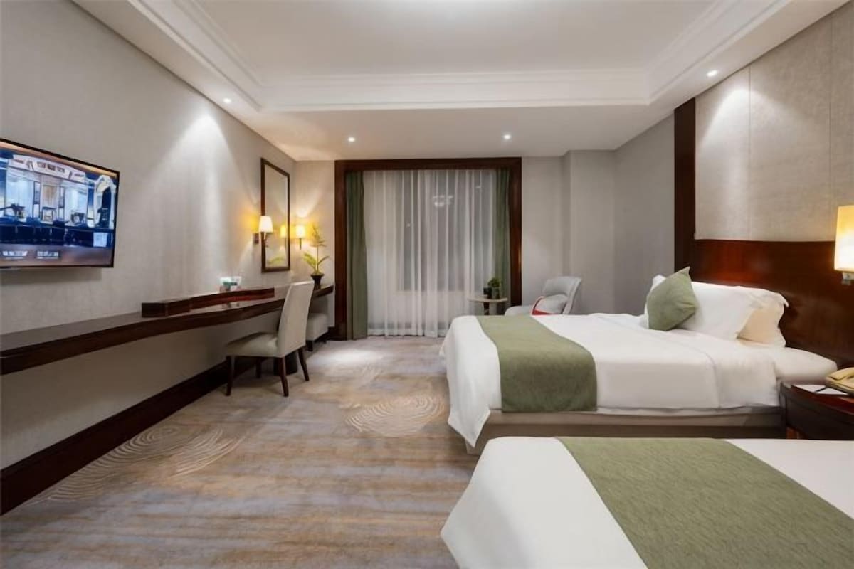 Habitación de hotel con cama, escritorio, silla, televisión y ventana con cortinas.