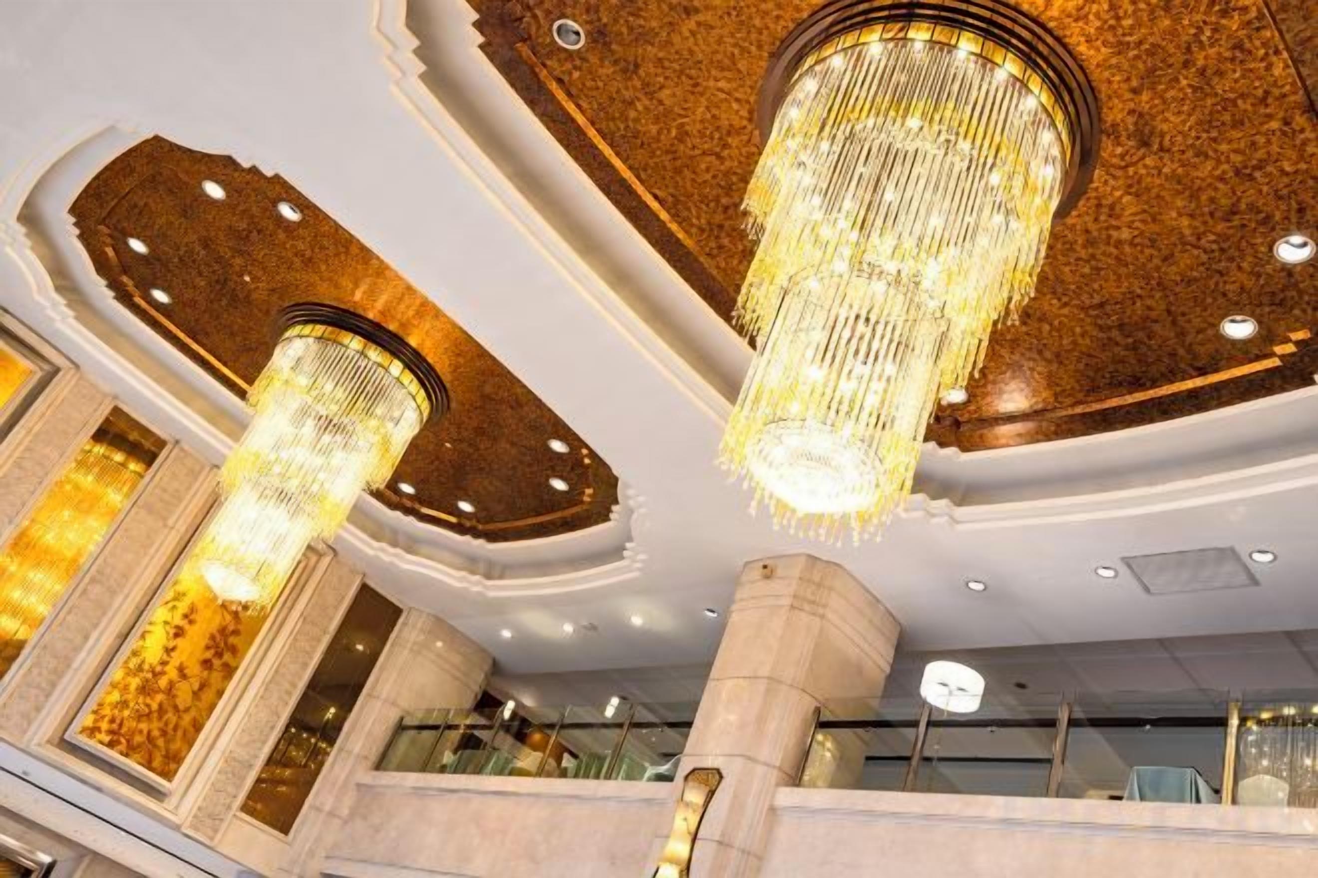 A lobby with chandeliers, columns, and a ceiling with a decorative pattern.