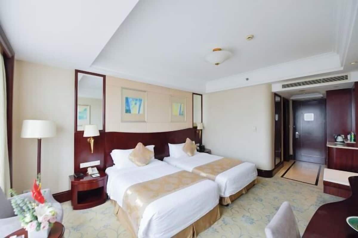 A hotel room with two beds, a desk, a chair, a mirror, and artwork on the wall.