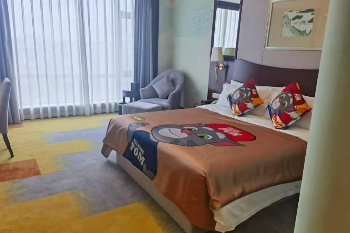 A hotel room with a bed, a chair, a lamp, and a window with curtains.