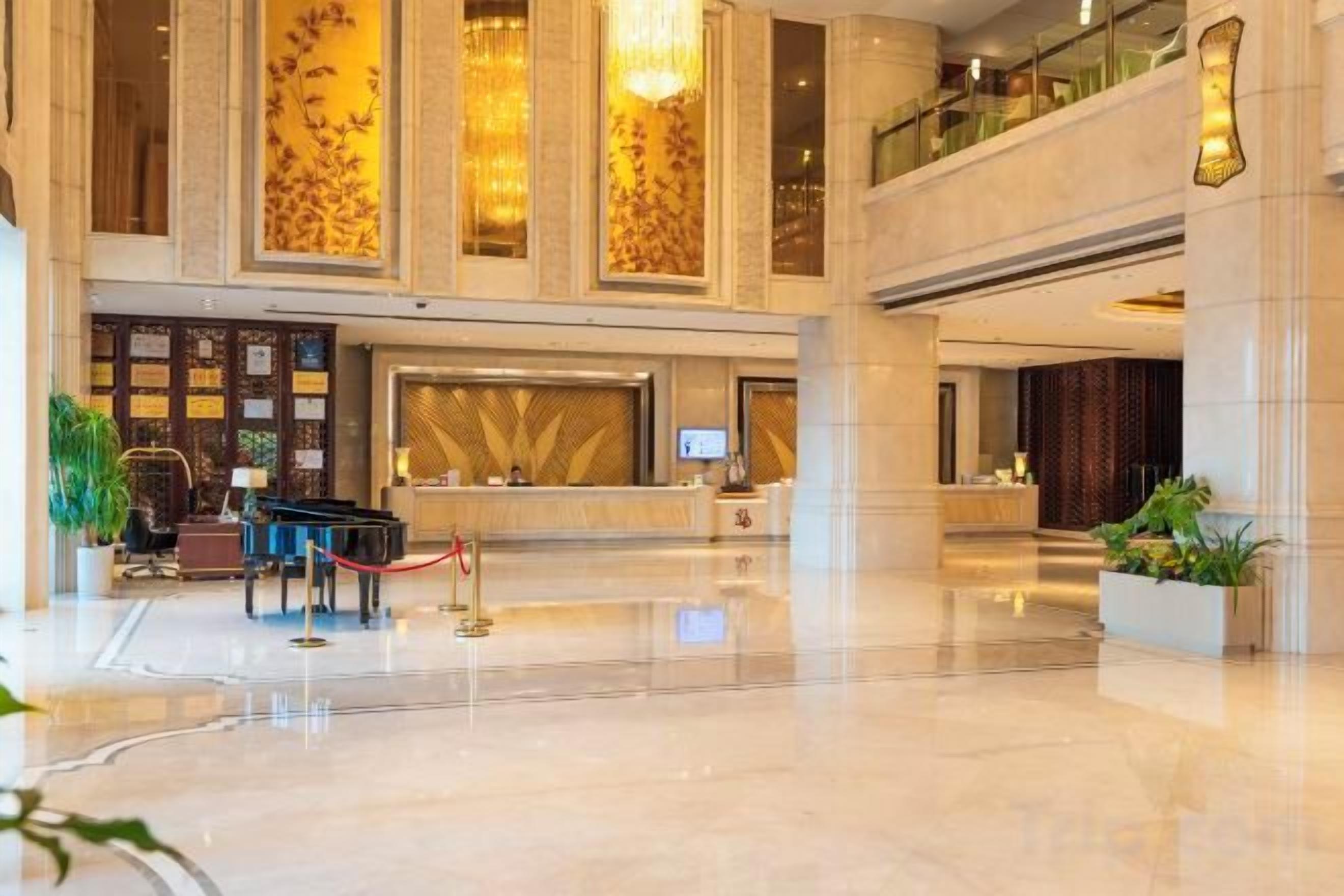 A spacious lobby with a reception desk, a piano, and a large chandelier.