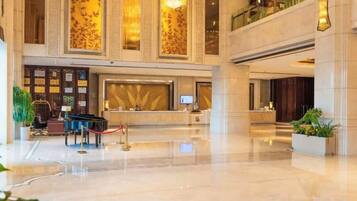 A spacious lobby with a reception desk, a piano, and a large chandelier.