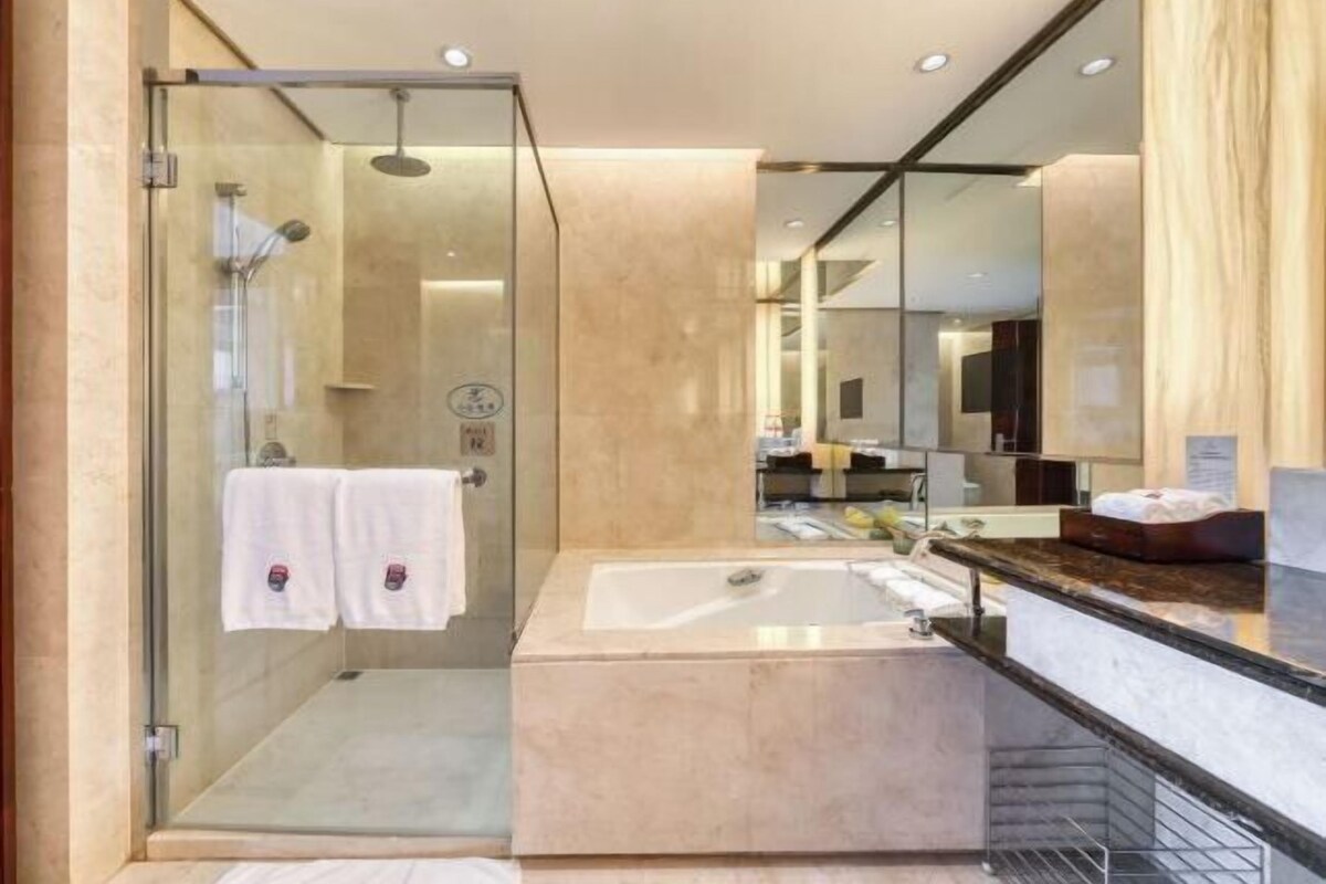 A modern bathroom with a glass-enclosed shower, a large mirror, and a marble sink.