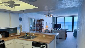 Una cucina moderna completa di lavastoviglie, un'area pranzo con tavolo e sedie, un soggiorno con divano e TV, e un balcone con vista sull'oceano.