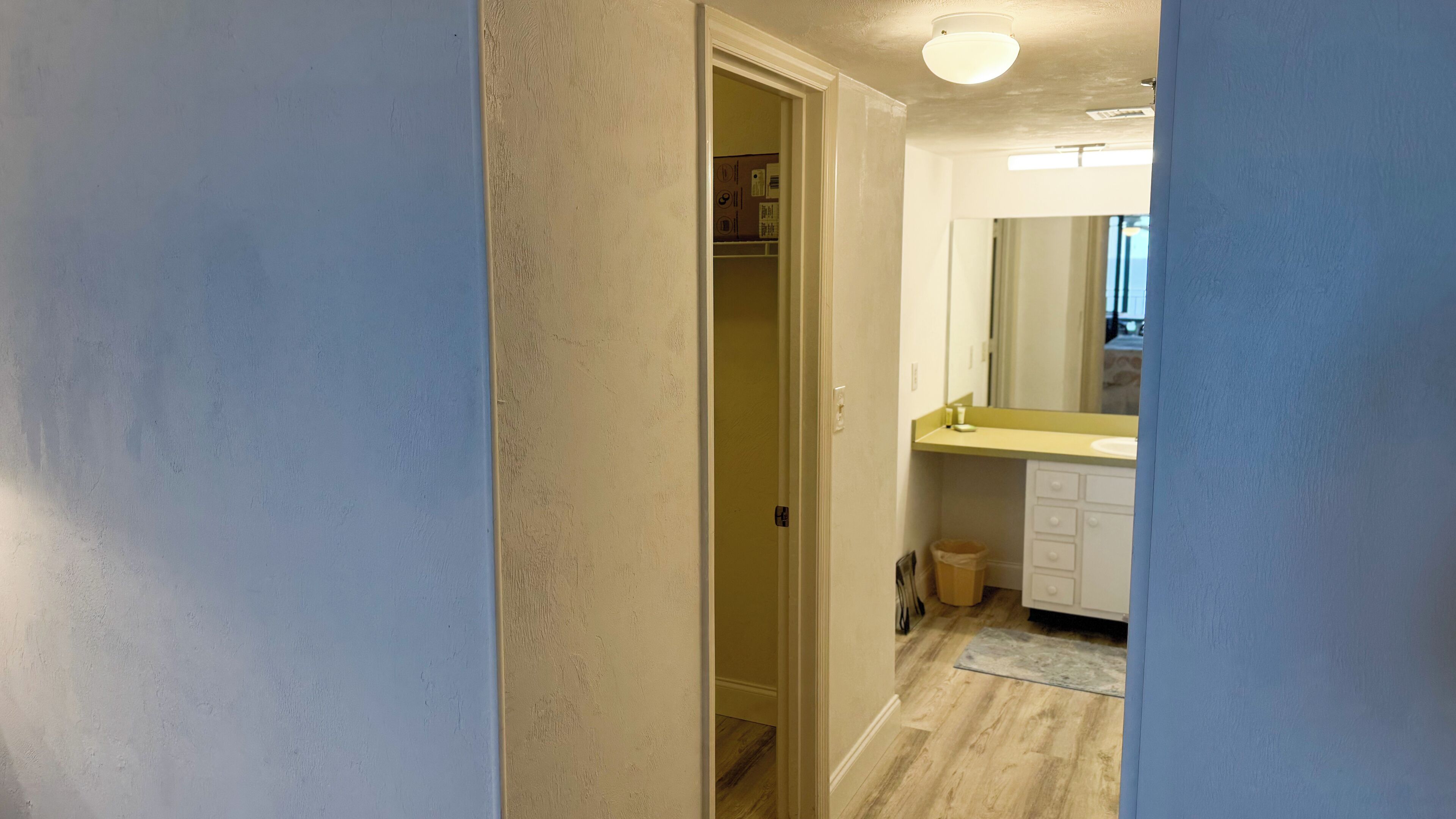 Un pasillo que conduce a un baño con espejo, lavamanos y cubo de basura.