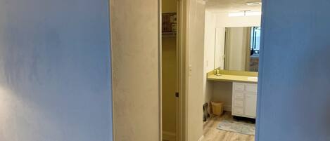Un pasillo que conduce a un baño con espejo, lavamanos y cubo de basura.
