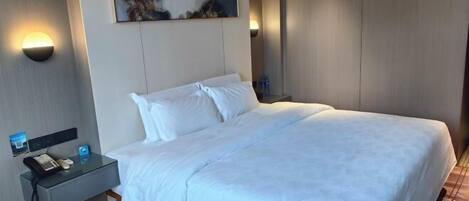 A hotel room with a large bed, a bedside table with a phone and a lamp, and a wall-mounted artwork.