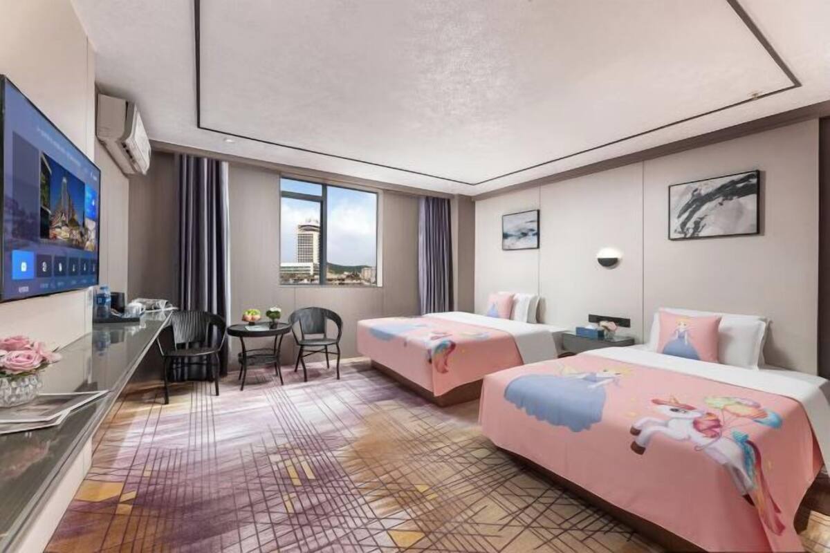A hotel room with two beds, a desk with a computer, a chair, and a view of the city.