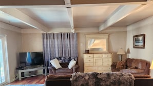 A living room with a sofa, a TV, a wooden floor, a window, and a lamp.