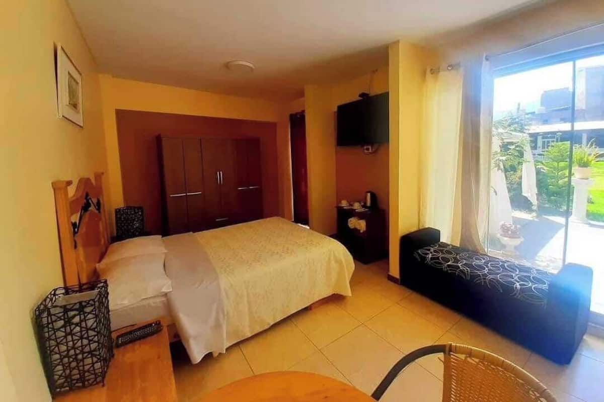 A hotel room with a bed, a small table, a chair, a TV, and a balcony with a view.