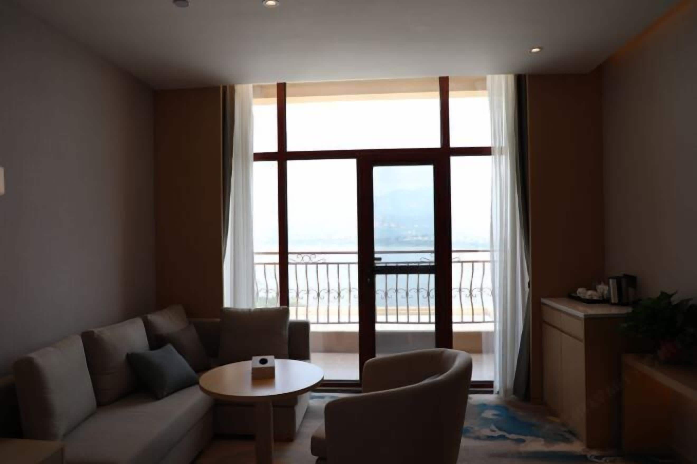 Una habitación de hotel moderna con balcón, sofá, una mesita y una silla.