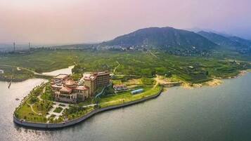 An island hotel with a large building, surrounded by water and greenery, with mountains in the background.