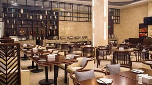 A spacious restaurant with multiple dining tables and chairs, a large pillar, and shelves with various items.