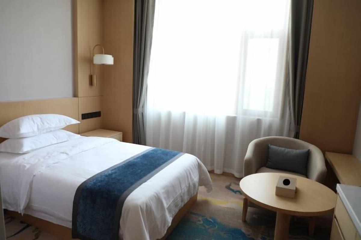 Et hotelværelse med en seng, en stol, et lille bord og en lampe.