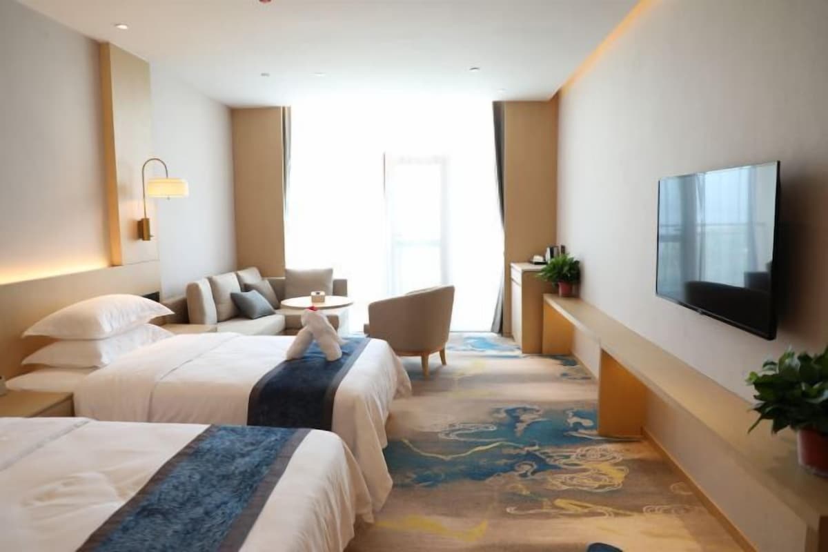 Et hotelværelse med to senge, et fjernsyn, et opholdsområde og et stort vindue.