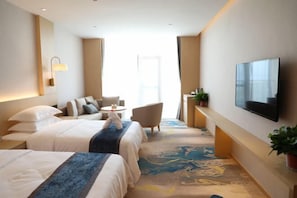 Habitació d'hotel amb dos llits, televisió, zona de seients i una finestra gran.