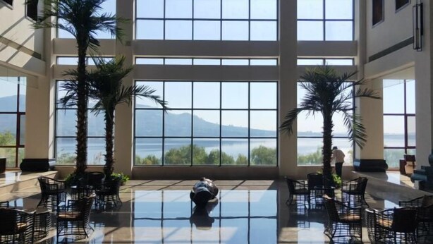 A spacious indoor area with a large glass window offering a view of a body of water and mountains.