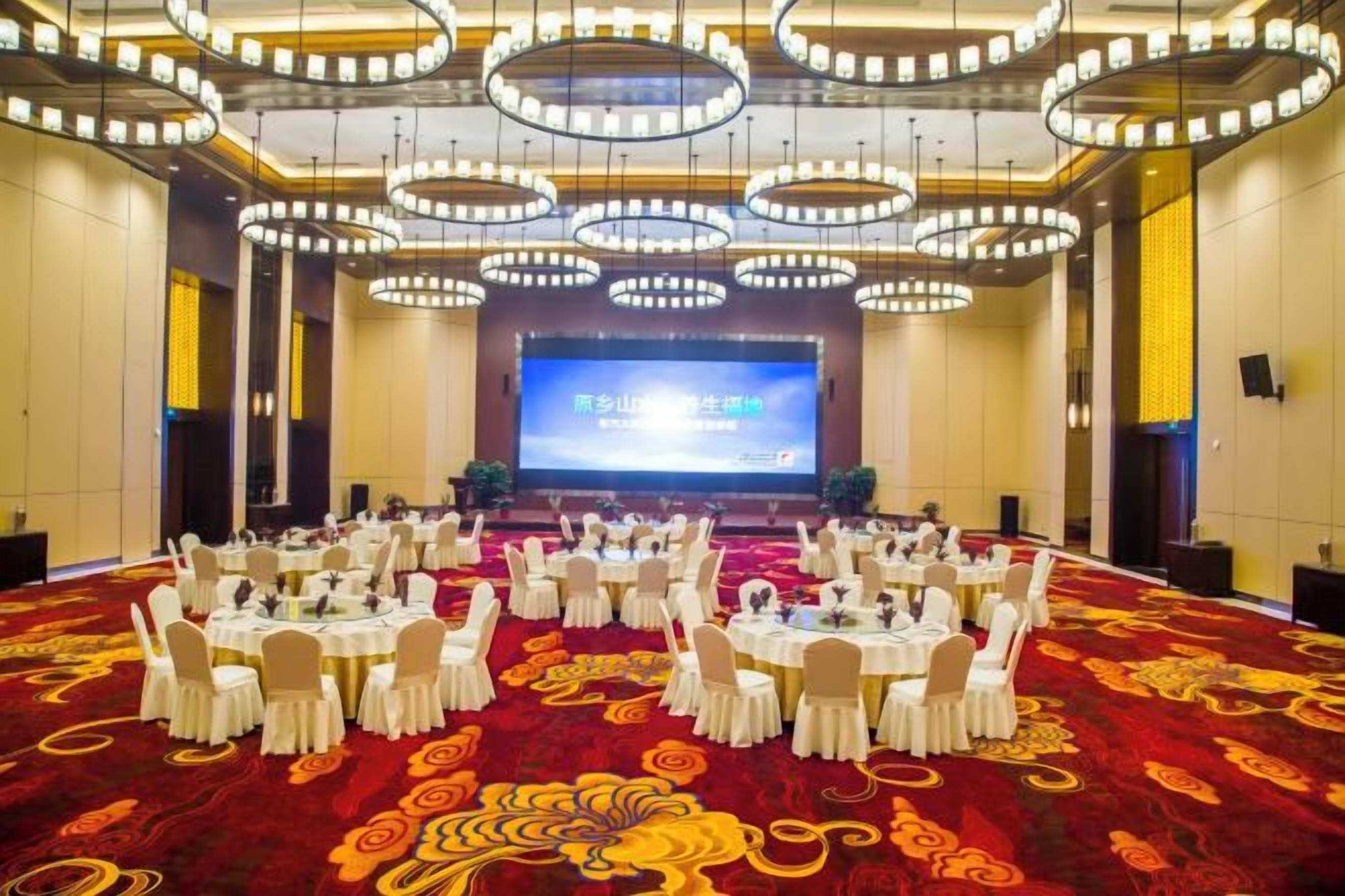 A conference room with round tables, chairs, and a large screen at the front.