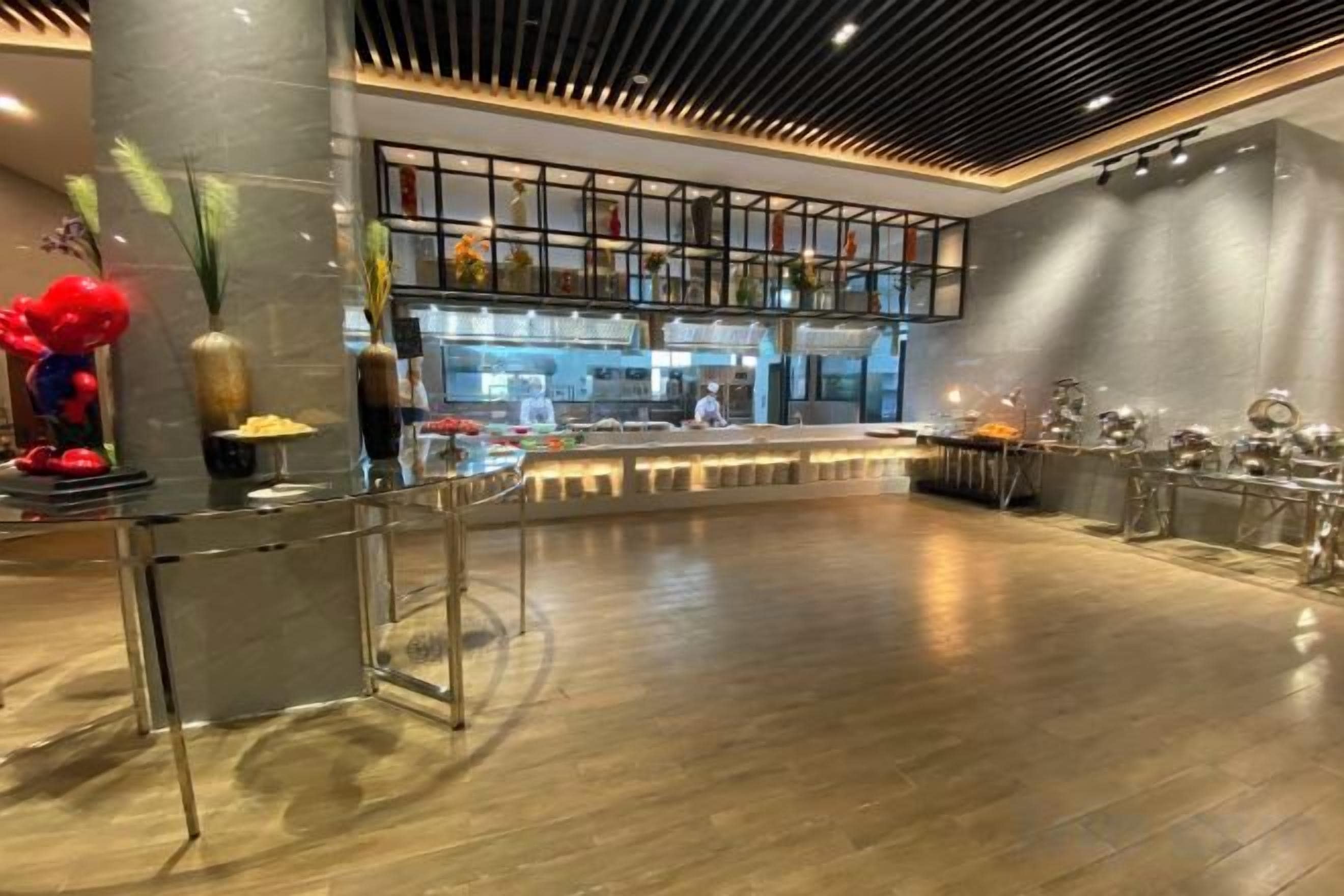 A spacious lobby with a central seating area, a kitchen in the background, and a modern ceiling design.