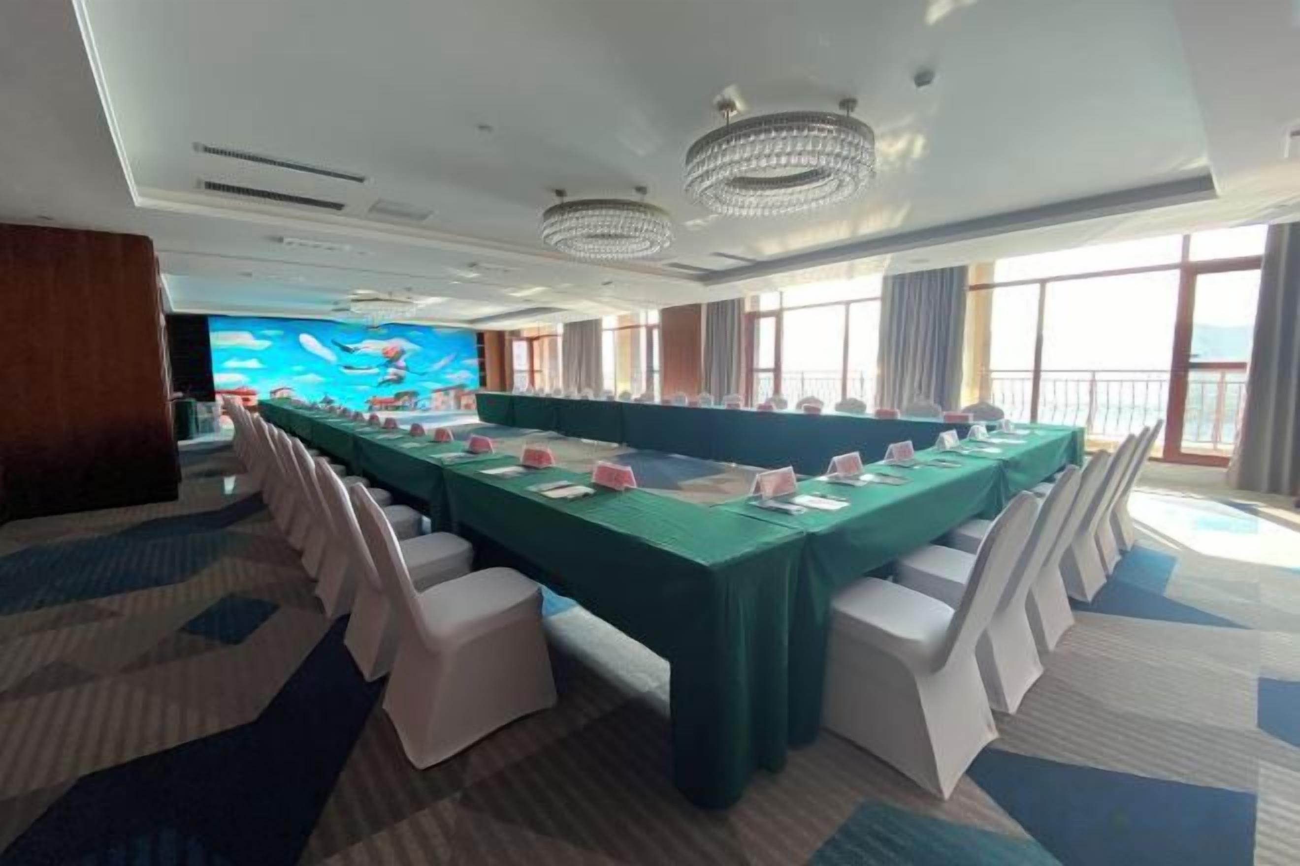 A conference room with a long table, white chairs, and a large screen.
