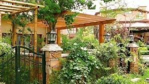A garden with a wooden pergola, stone pillars, and a metal gate.