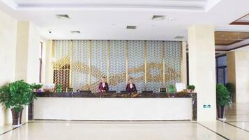 Un mostrador de recepción con dos empleados, una pared estampada y plantas en macetas.