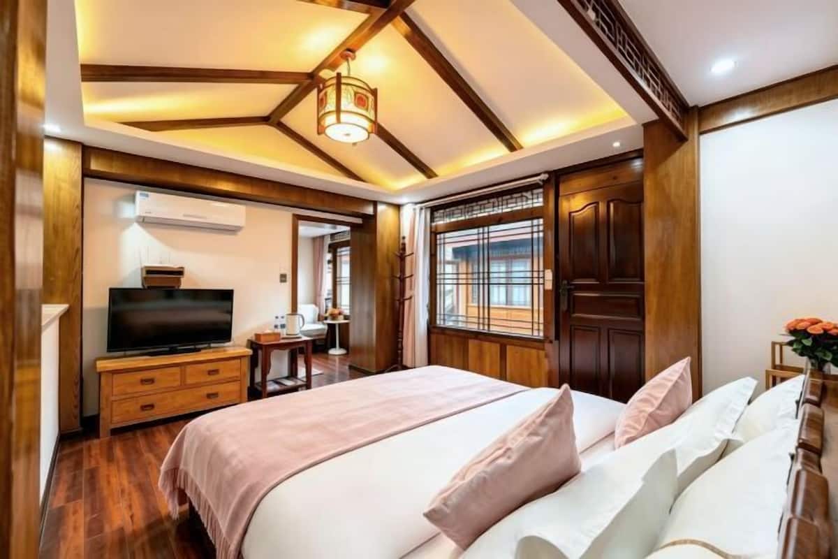 Un dormitorio con una cama grande, techo de madera, televisor y ventana con persianas.