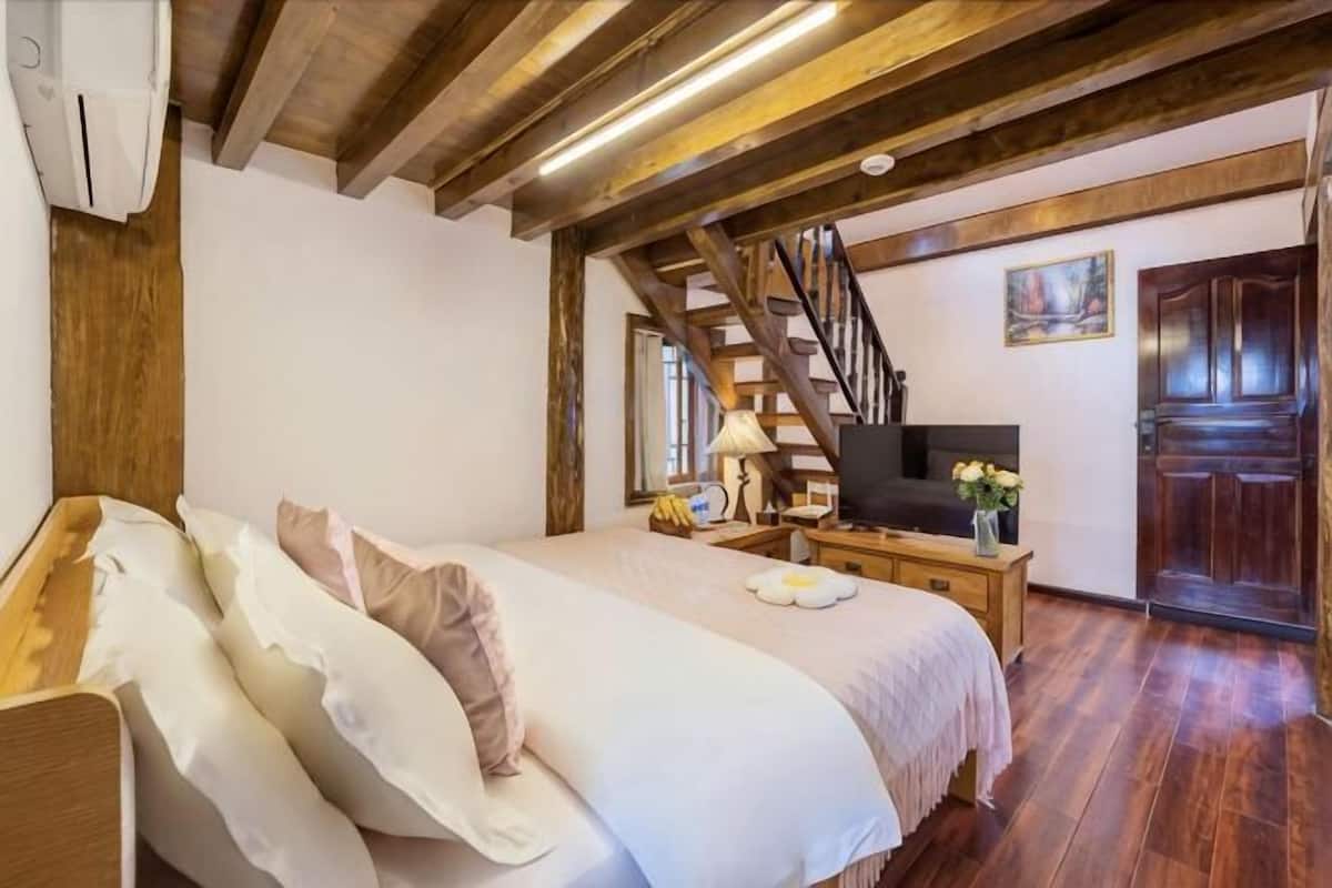 Un dormitorio con cama, vigas de madera, televisor, mesita de noche y una puerta.