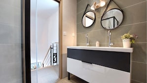 Ein modernes Badezimmer mit einem weißen Waschtisch, zwei Spiegeln, einem Waschbecken und einer Topfpflanze.