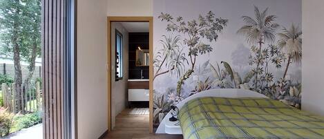 Un dormitorio con una cama grande, un mural de plantas tropicales en la pared y suelo de madera.