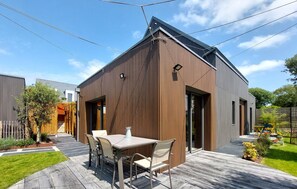 Una casa moderna con fachada de madera, una terraza con mobiliario exterior y un cielo despejado.