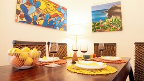 Mesa de jantar posta com pratos, copos e um recipiente com limões. Duas pinturas adornam a parede acima da mesa.