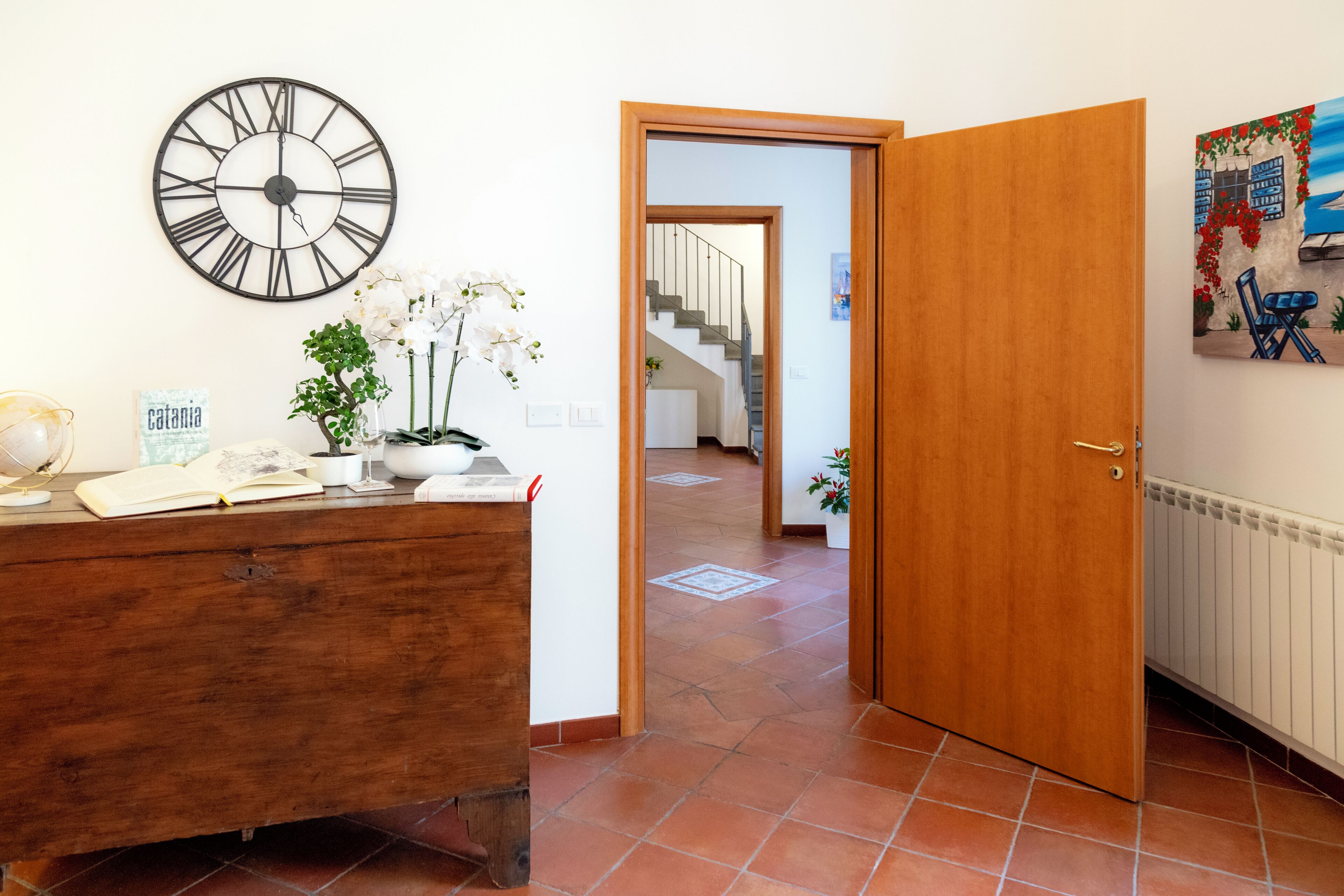 Een kamer met een houten bureau, een wandklok, een kamerplant en een deur naar een andere kamer.