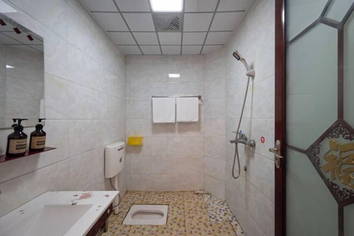 Une petite salle de bain avec des toilettes, un lavabo et une douche. On trouve des articles de toilette sur le comptoir et une serviette est accrochée au mur.