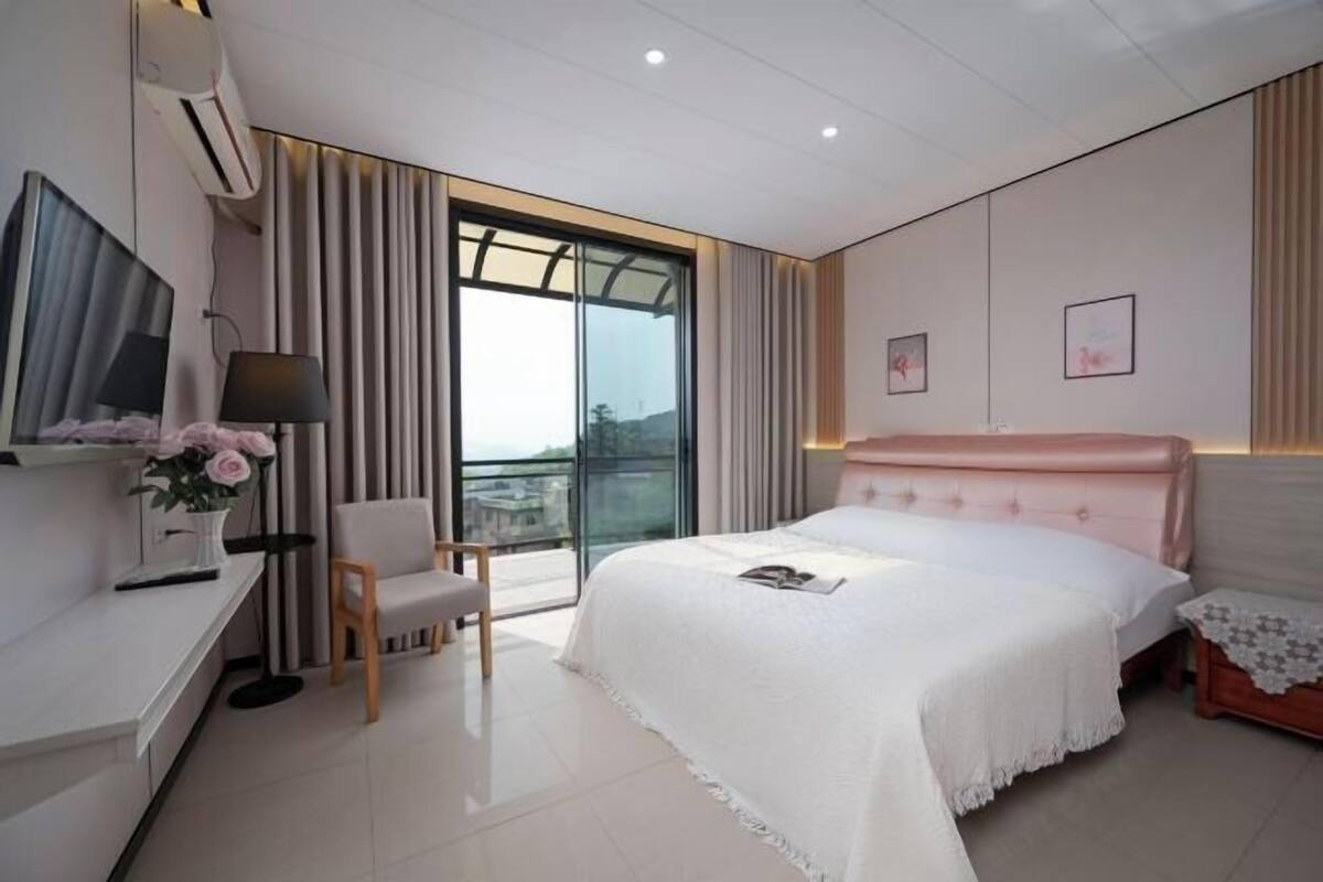Une chambre moderne avec un grand lit, un bureau, une chaise et un balcon agrémenté de rideaux.