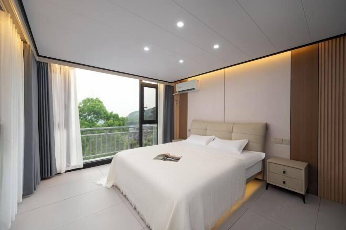Une chambre moderne avec un grand lit, des tables de chevet et une vue sur l’extérieur grâce à une porte-fenêtre coulissante.