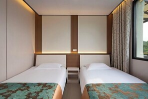 Een hotelkamer met twee bedden, een tafeltje en een raam met gordijnen.