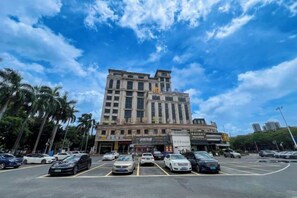 A multi-story hotel with a modern facade, a parking lot in front, and palm trees lining the street.