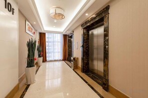 A hotel hallway with a marble floor, a large elevator, and a potted plant. - Dihao Hotel (Guangzhou Panyu Shiqiao Aoyuan Plaza) (Guangzhou)
