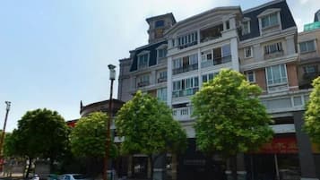 A multi-story building with balconies, a clear sky, and trees along the street.