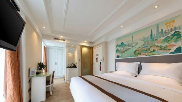 A hotel room with a large bed, a desk, a chair, and a painting on the wall. - Dihao Hotel (Guangzhou Panyu Shiqiao Aoyuan Plaza) (Guangzhou)