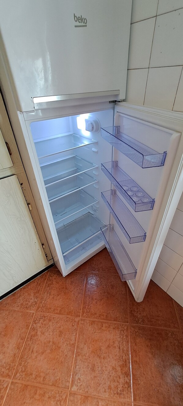 Un réfrigérateur blanc, doté de plusieurs étagères et d’un compartiment congélateur, situé dans une cuisine dont le sol est carrelé.