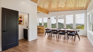 Une salle à manger spacieuse avec un plafond en bois et de grandes fenêtres offrant une vue sur les montagnes.