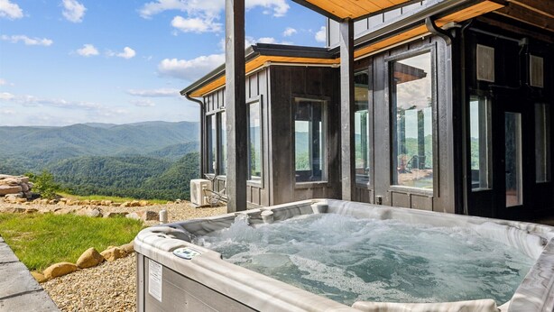 Un bain à remous avec vue sur les montagnes, une terrasse en bois et de grandes fenêtres.