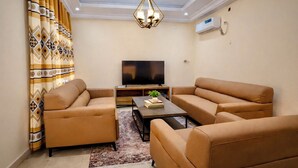 Un salon comprenant un ensemble de canapés, un téléviseur à écran plat, une table basse et un rideau à motifs.