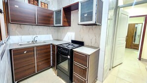 Une cuisine de taille réduite, dotée de meubles de rangement en bois foncé, d’une cuisinière encastrée et d’une hotte aspirante.