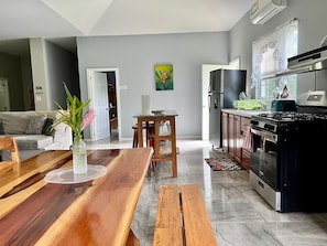 A modern kitchen with a stove, oven, and dining area with a wooden table and benches. - Charming 3-bedroom Villa-5 beds-AC - 7minutes drive to San Ignacio- Restaurant (Belize)